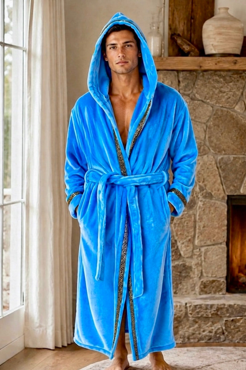 A man wearing a bright blue plush hooded bathrobe with gold patterned trim, standing in front of a stone fireplace with a fire burning inside.