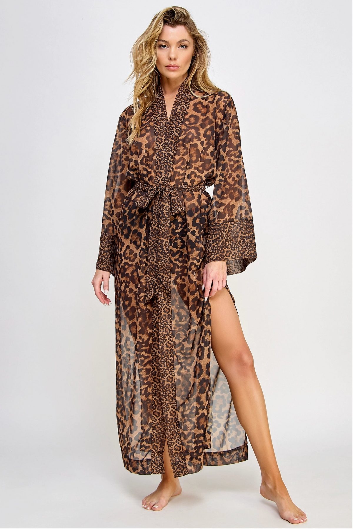 A woman modeling a long leopard-print robe with a tie waist and high side slit, photographed against a plain light gray studio background.