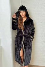 Woman wearing a black hooded Royalty Robe with gold Greek key trim and pockets. Soft bathrobe with hood for women.